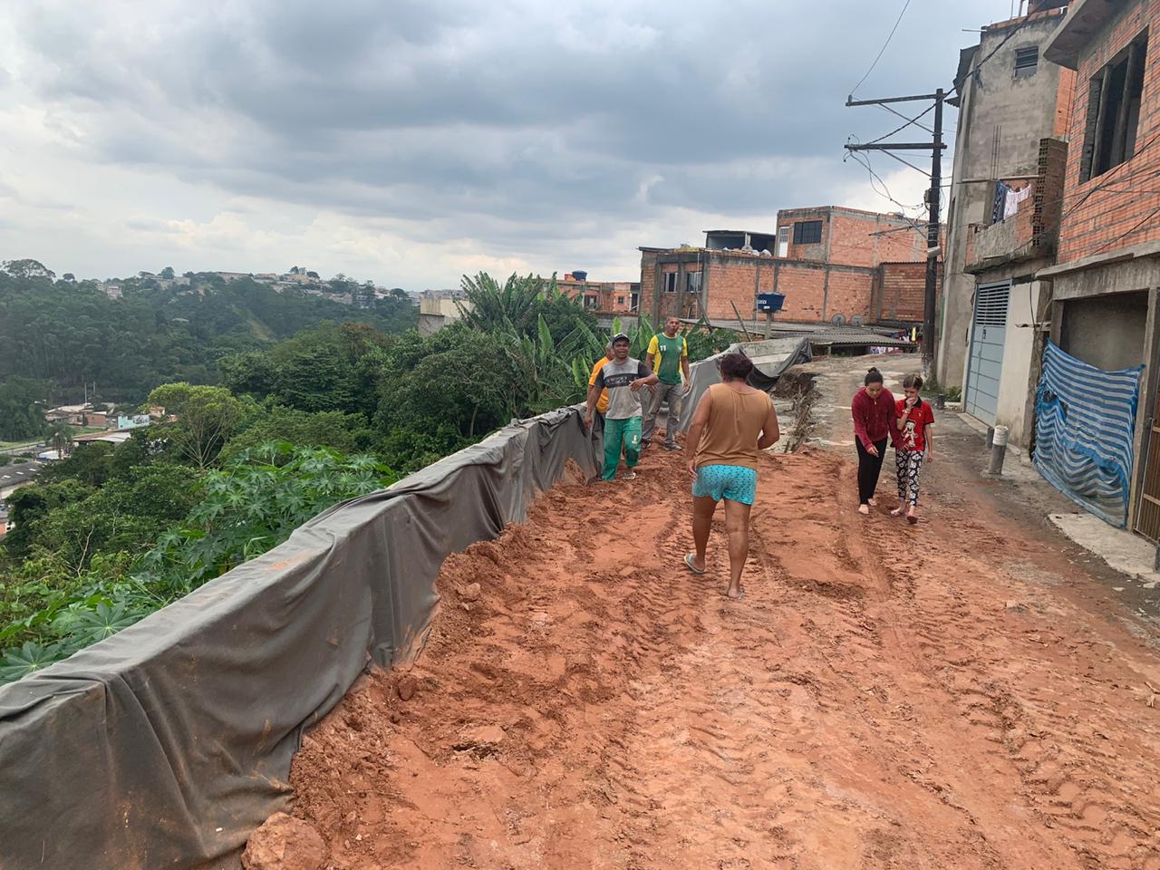 Rua com a parede de contenção de deslizamentos construída e terra vermelha, firme, sendo jogada